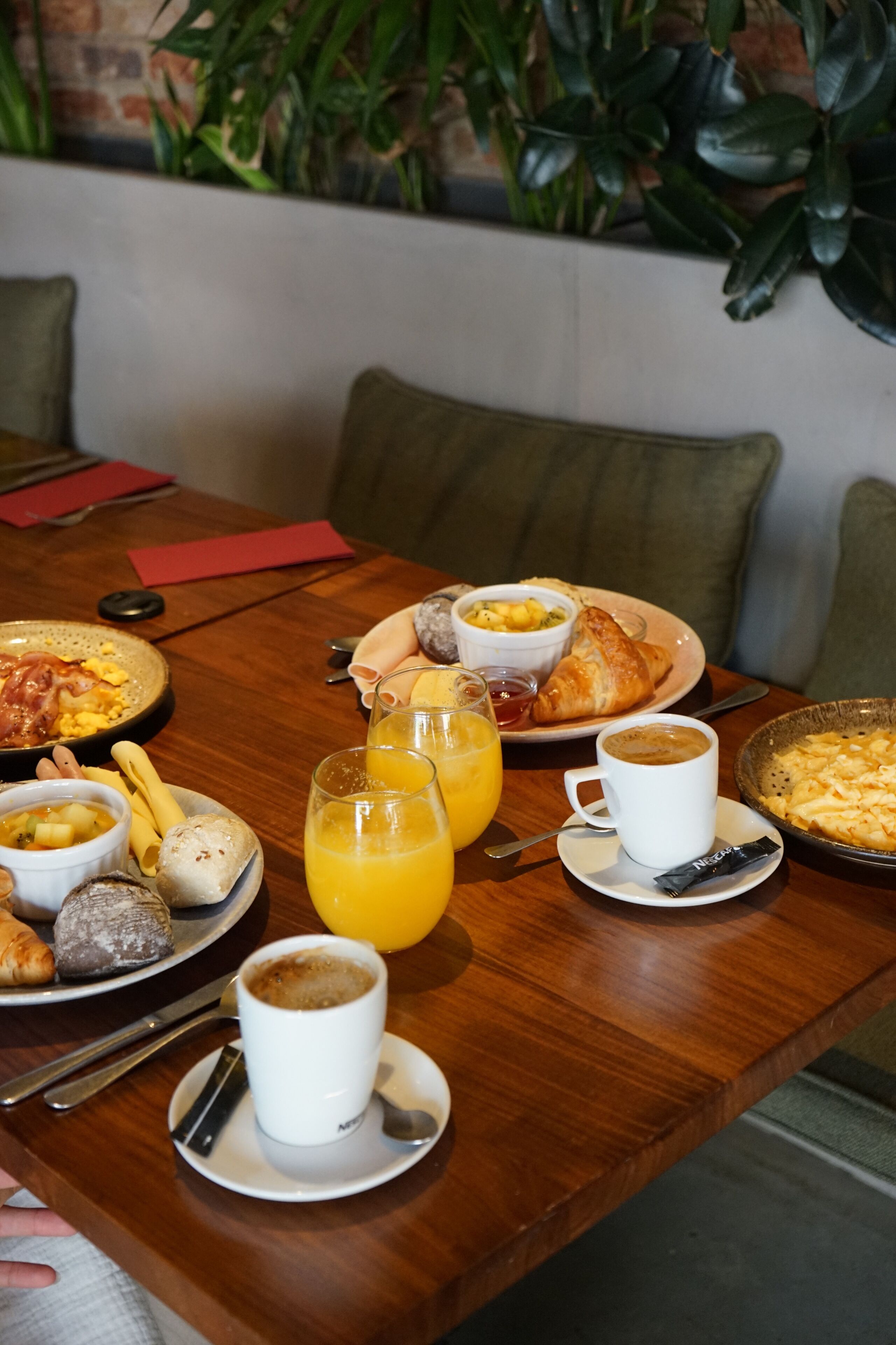 A wooden dining table with breakfast items including croissants, fruit, and coffee.