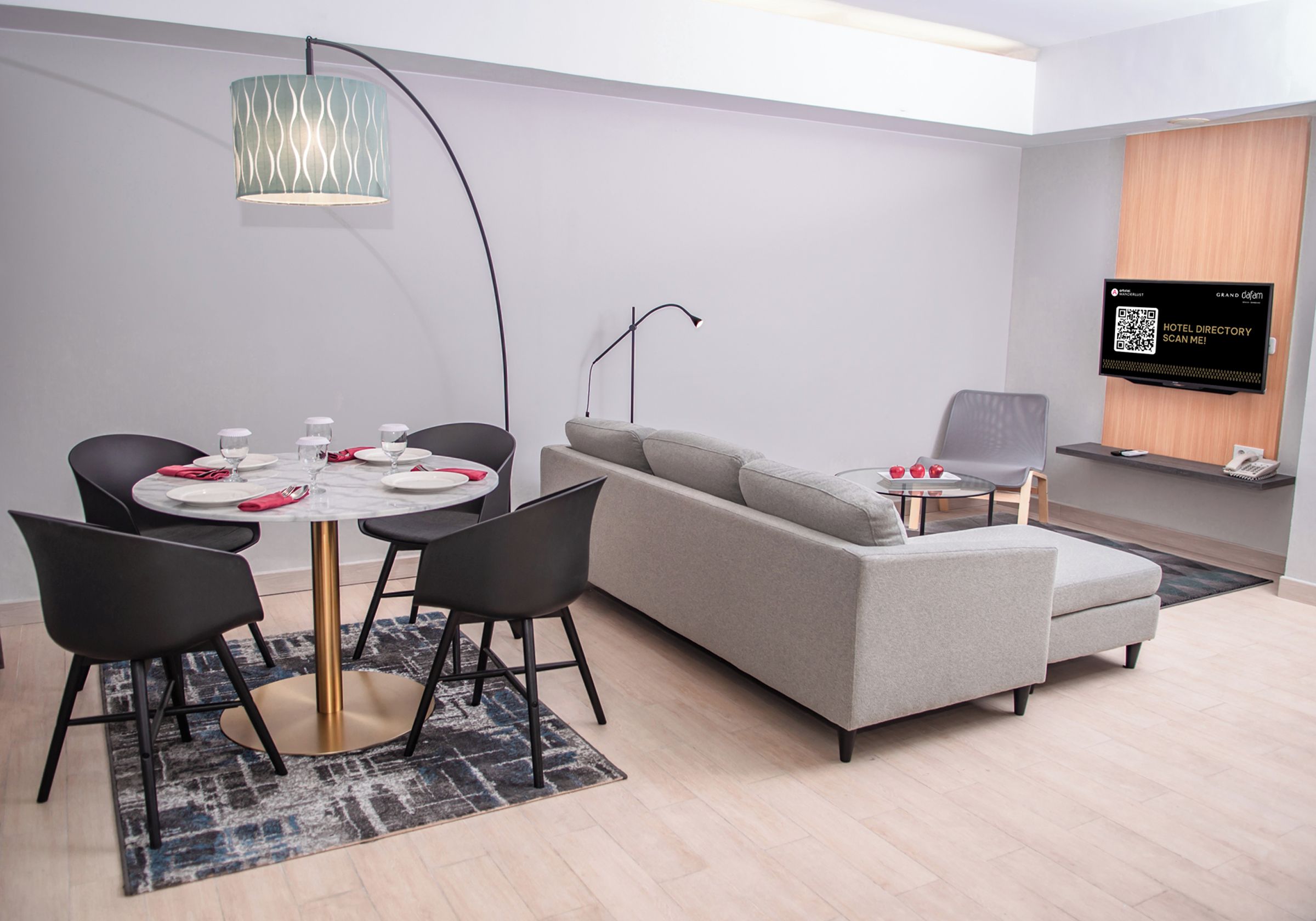 Quarto de hotel moderno com área de refeições, sofá, TV e um código QR para o diretório do hotel.
