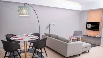 Quarto de hotel moderno com área de refeições, sofá, TV e um código QR para o diretório do hotel.