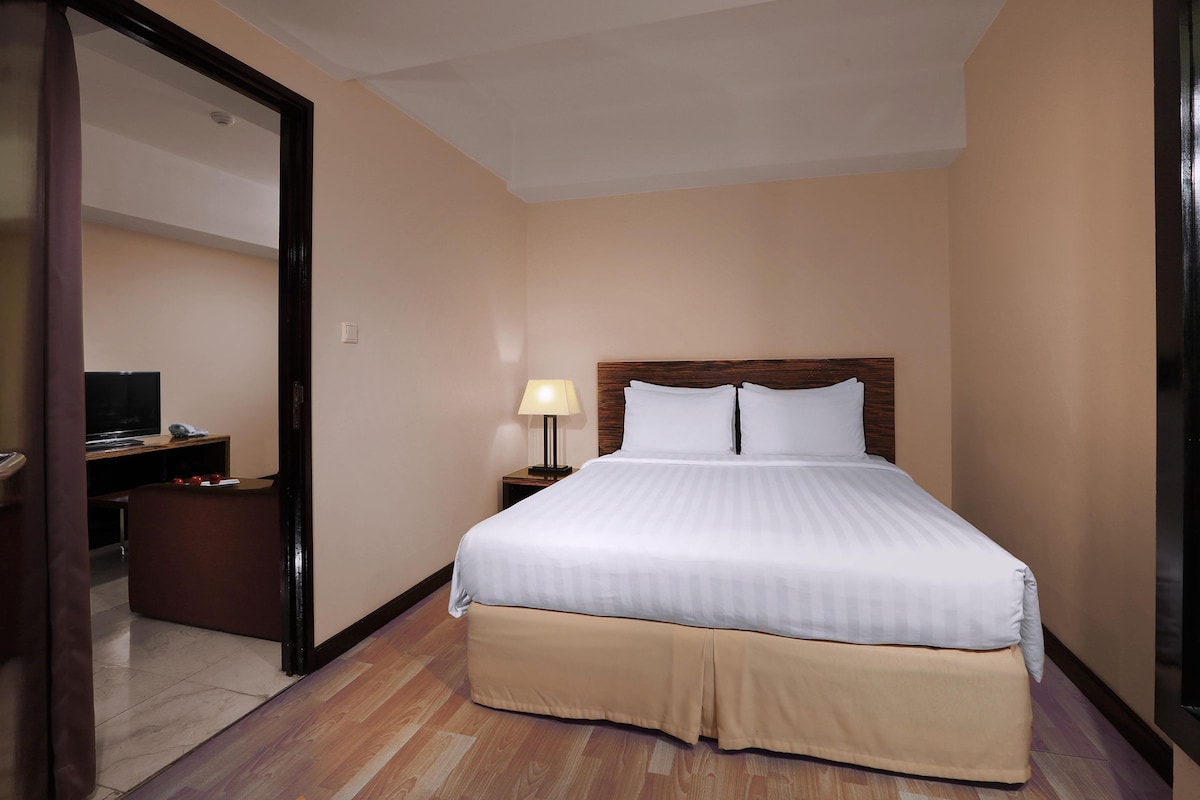 Una camera d'albergo con un letto grande, una scrivania con una lampada e una televisione.