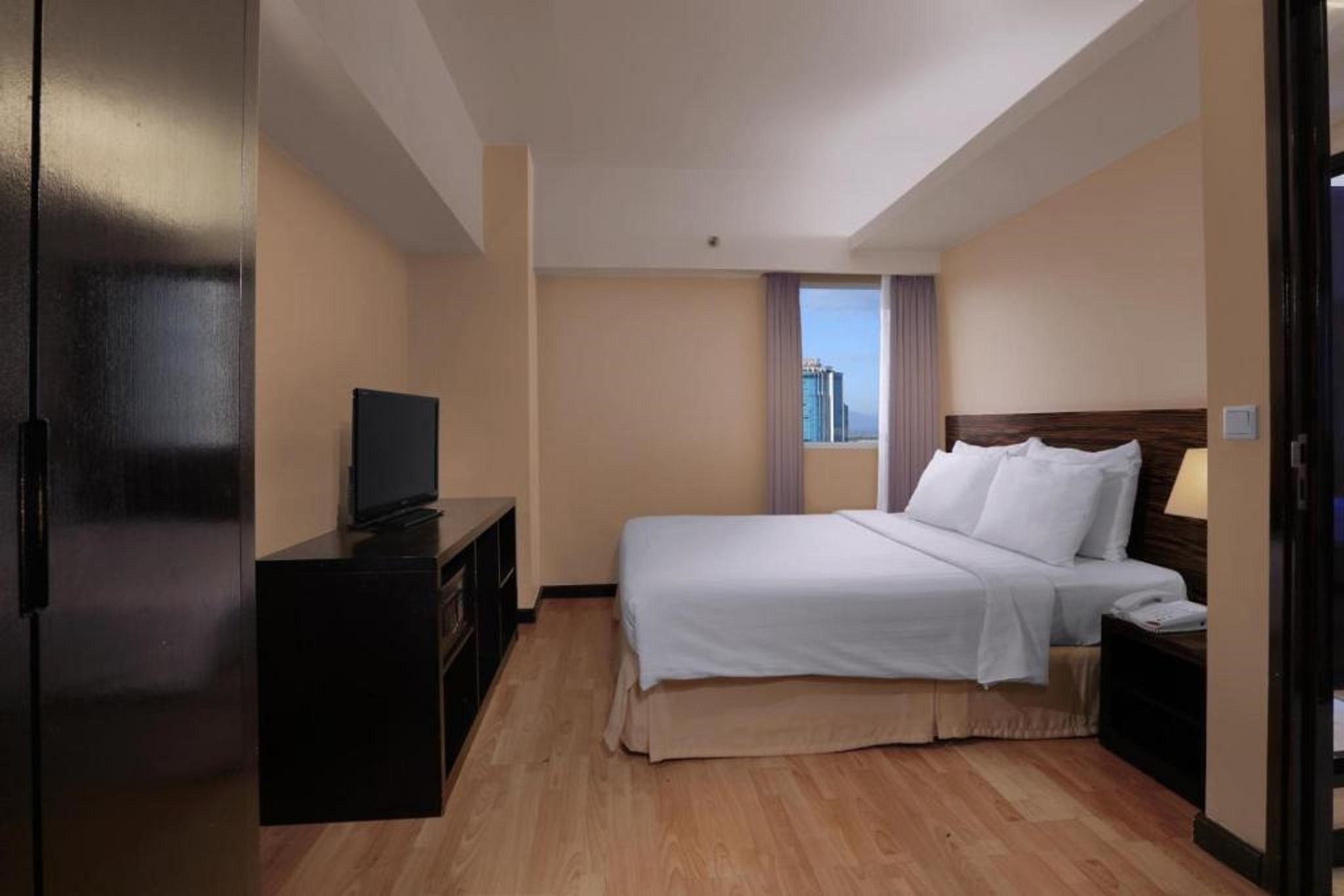 Una habitación de hotel con cama, televisión en una cómoda, ventana con vistas y una puerta.