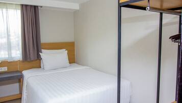 Ein Hotelzimmer mit Bett, Nachttisch, Kleiderschrank und einem fenster mit Vorhängen.