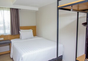 A hotel room with a bed, a bedside table, a wardrobe, and a window with curtains.