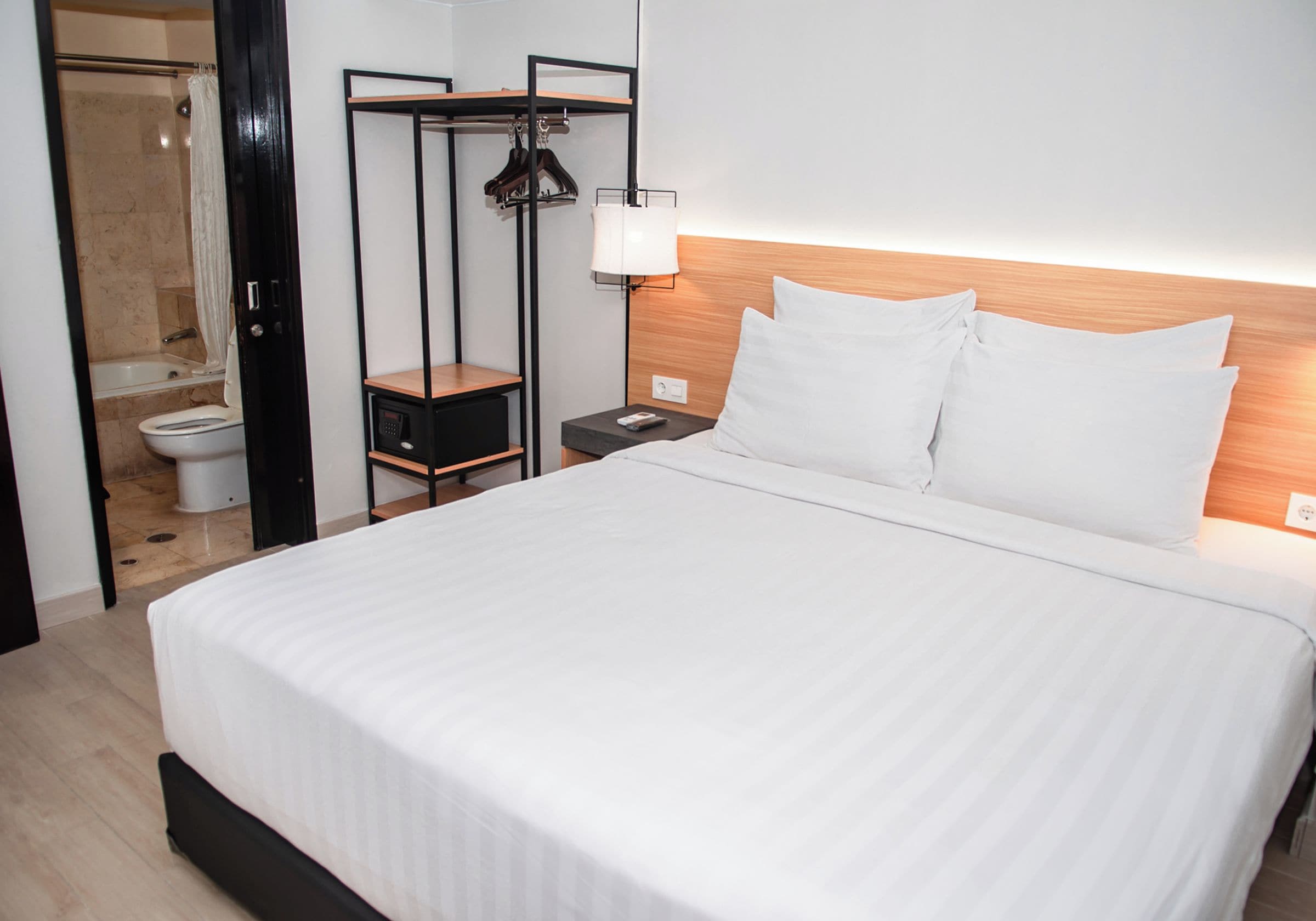 Hotelkamer met een bed, nachtkastje, lamp, kledingkast en een badkamer die door een open deur zichtbaar is.