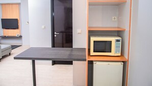 Un espacio habitable compacto con kitchenette, un televisor de pantalla plana montado en la pared, un refrigerador pequeño y un microondas en un estante.