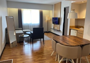 Une chambre d’hôtel avec un plancher en bois, un canapé, une table à manger avec des chaises, un téléviseur fixé au mur et un petit coin cuisine.