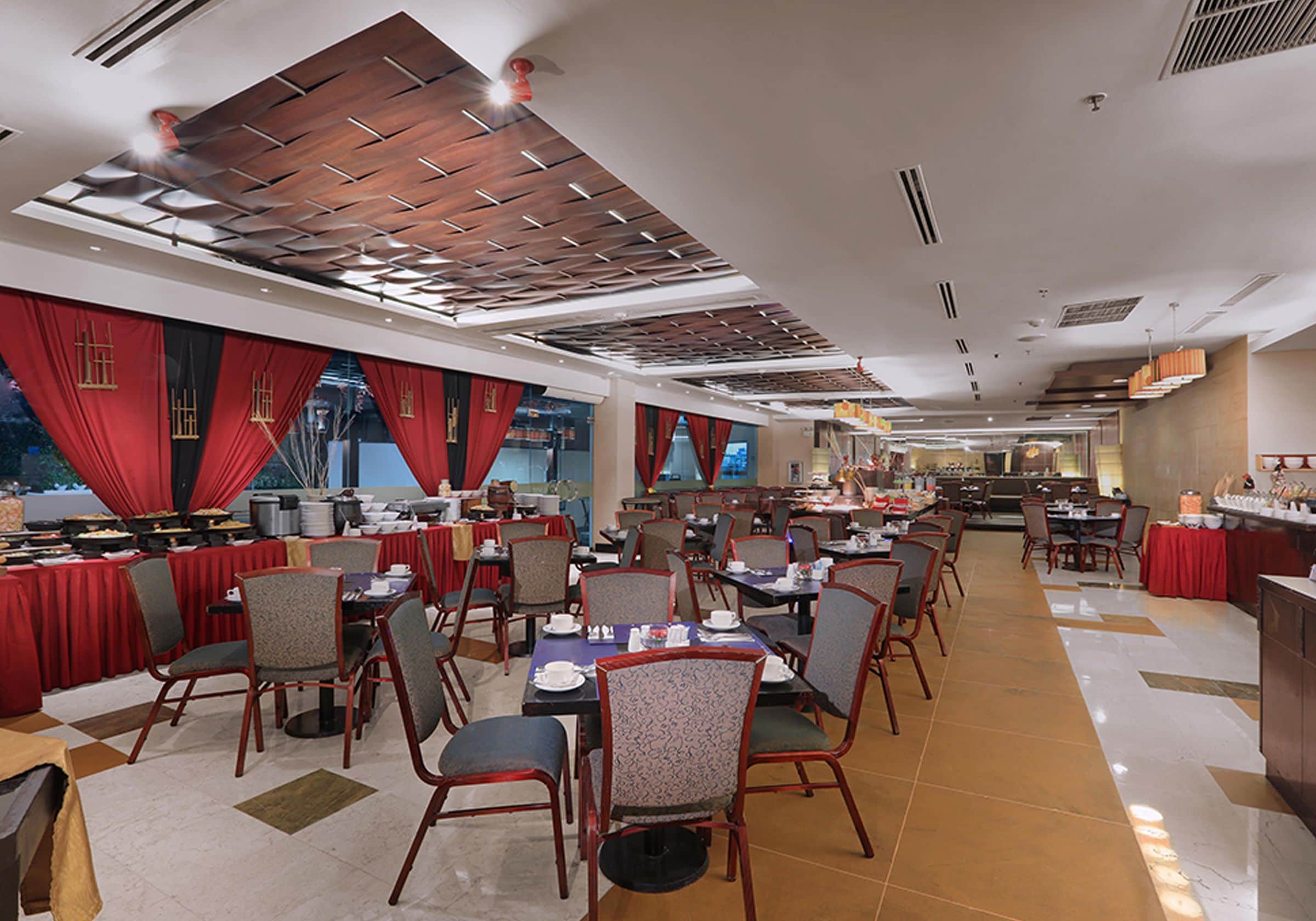 A spacious dining area with multiple tables and chairs, a high ceiling with wooden paneling, and a view of the dining area through large windows.