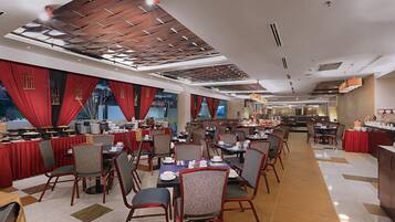 A spacious dining area with multiple tables and chairs, a high ceiling with wooden paneling, and a view of the dining area through large windows.
