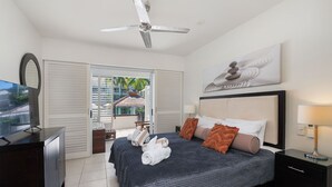 A modern bedroom with a bed, a ceiling fan, a TV, and a view of a resort. - Beach Club Lagoon View 2 Bedroom Apartment 3113-4 (Palm Cove)