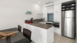 A modern kitchen with white cabinets, a stainless steel refrigerator, and a dining area with a black table and wicker chairs. - Beach Club Lagoon View 2 Bedroom Apartment 3113-4 (Palm Cove)