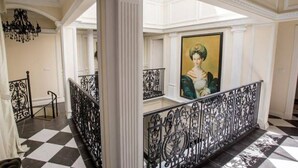 Un amplio pasillo con suelo a cuadros, barandillas negras ornamentales y un cuadro grande enmarcado en la pared.