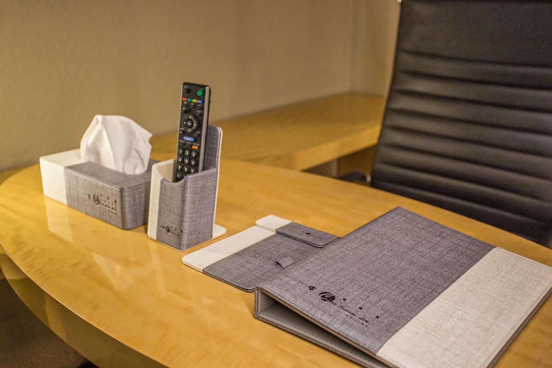 A hotel room with a wooden table, a remote control holder, a tissue box, and a notebook.