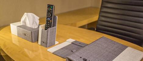 A hotel room with a wooden table, a remote control holder, a tissue box, and a notebook.