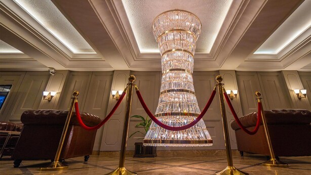 En storslagen kristallkrona i en hotelllobby, med röda sammetsband och guldfärgade ståndare.