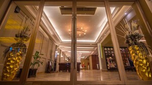 En hotellobby med modern design, med en stor kristallkrona i mitten, dekorativa växter och ett polerat marmorgolv.