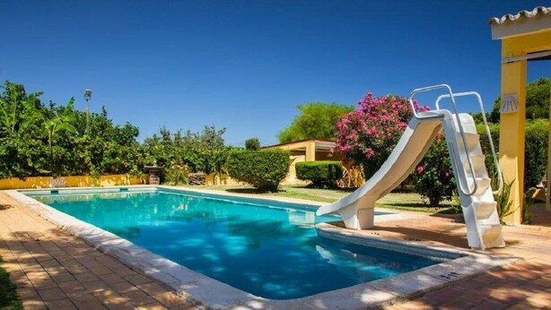 Piscina con tobogán, rodeada de vegetación y un cielo despejado.