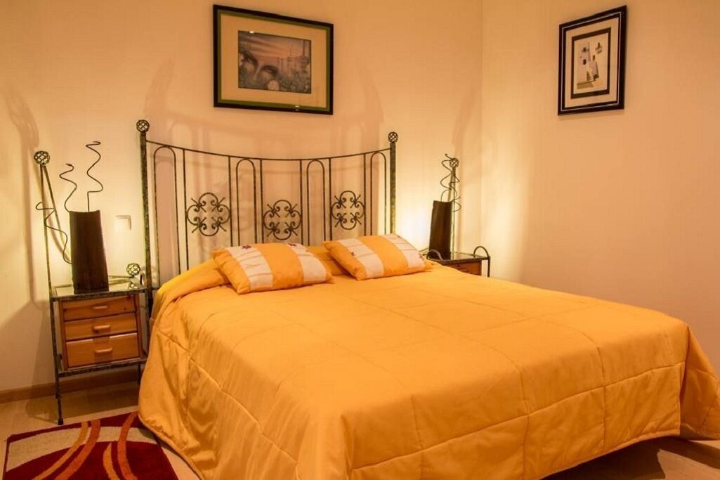 A bedroom with a bed, two bedside tables, a nightstand, a framed picture on the wall, and a red and white patterned rug.