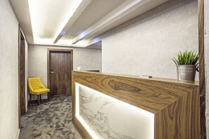 A reception area with a wooden reception desk, a marble inlay, a yellow chair, and a potted plant. - Nomad Luxury Suites (Belgrade)