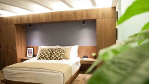 Un dormitorio moderno con cabecera de madera, una cama grande con cubrecama color beige, una mesita de noche con lámpara y un cuadro enmarcado.