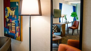 Habitación de hotel de diseño moderno, con un cuadro abstracto grande, una lámpara de pie, un sofá, una mesita y un televisor.