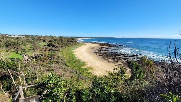 Un paysage côtier caractérisé par une plage de sable, une côte rocheuse et une végétation luxuriante.