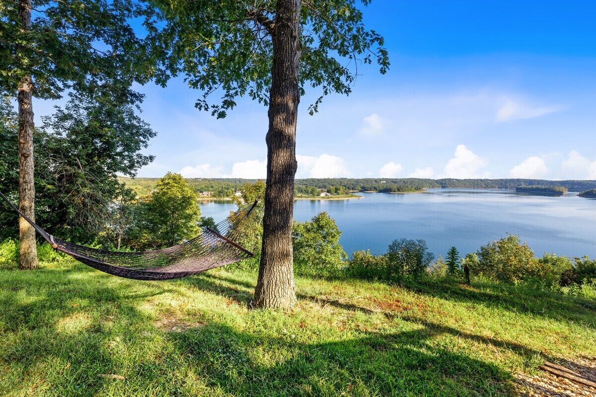 Eine Hängematte zwischen Bäumen mit Blick auf einen See unter blauem Himmel.