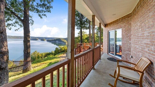 Ein Balkon mit Blick auf einen See und Bäume, Holzmöbel und eine Ziegelwand.