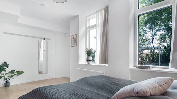 Quarto com cama grande, janela com vista para árvores, radiador e planta em vaso.