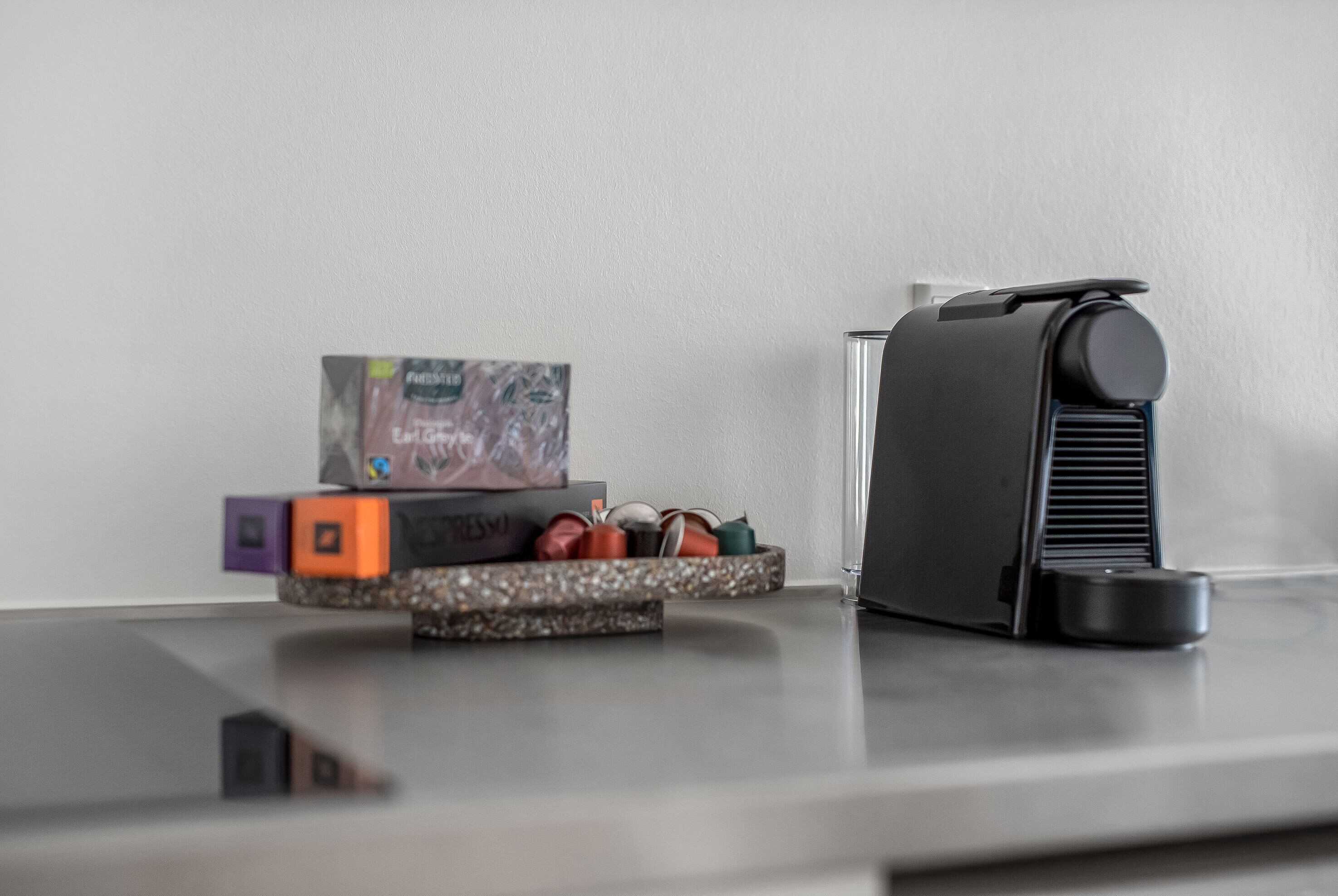 A modern kitchen with a coffee machine, a small shelf with a box and some colorful items, and a countertop.