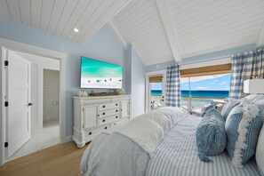 A bedroom with a large bed, a television, a dresser, and a view of the ocean.