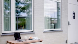 A laptop on a wooden table with a bowl of croissants and a cup, positioned by a window with a view of greenery. - Studio Apartment for 2 (København)