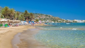 A beach with clear water, palm trees, and beach umbrellas. - Soleil Rooms & Suites (Hersonissos)