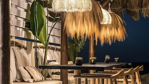 A cozy seating area with a thatched ceiling, a woven light fixture, and a small table with potted plants. - Soleil Rooms & Suites (Hersonissos)