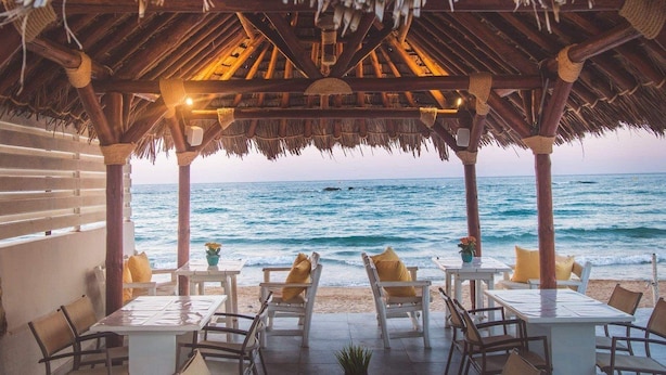 A beachside restaurant with thatched roof, white tables, and yellow cushions. - Soleil Rooms & Suites (Hersonissos)