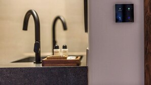 A modern bathroom with a sleek black faucet, a wooden tray, and a wall-mounted control panel with illuminated icons. - Soleil Rooms & Suites (Hersonissos)