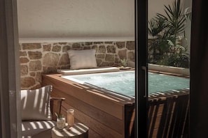 A spa area with a stone wall, a wooden bench, a cushioned chair, and a hot tub. - Soleil Rooms & Suites (Hersonissos)