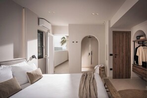 A modern bedroom with a large bed, a wooden door, and a walk-in closet. - Soleil Rooms & Suites (Hersonissos)