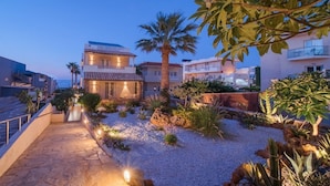 A coastal hotel with a stone pathway leading to a building with a tiled roof. - Soleil Rooms & Suites (Hersonissos)
