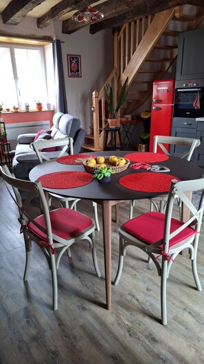 Un comedor con una mesa redonda, individuales rojos y sillas blancas con cojines rojos.