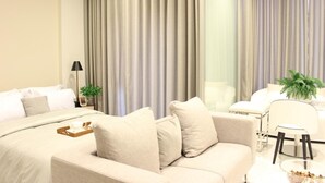 A modern hotel room with a large bed, a sofa, a dining area, and a large window with curtains. - Ariva Hyde Sukhumvit 11 - Adults Only (Bangkok)
