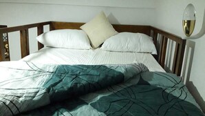 Una cama bien hecha con una manta verde estampada y almohadas blancas, un cabecero de madera y una lámpara de pared.
