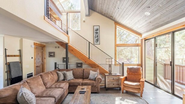 A spacious living area with a large sectional sofa, a wooden coffee table, and a leather armchair. A staircase with a wooden railing leads to an upper level. - MST #1-Large townhome in heart of town. Easily sleeps 10! Beautifully updated (Mammoth Lakes)