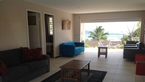 A spacious living room with a sofa, a blue armchair, a wooden coffee table, and a view of the ocean through large windows.