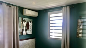 A bedroom with teal walls, a bed, a window with blinds, and an air conditioning unit.