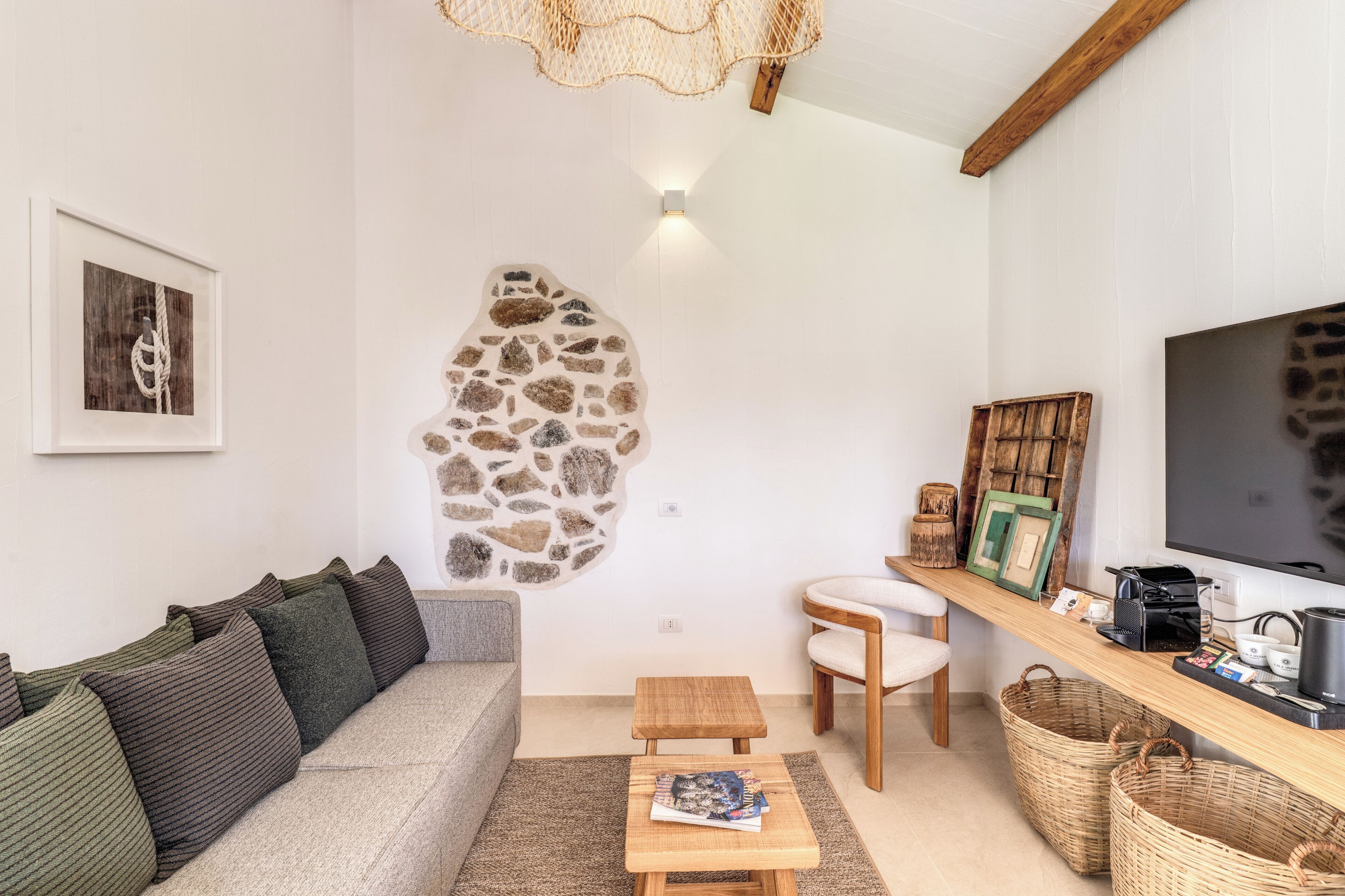 Un salon chaleureux avec un élément décoratif mural en pierre, un canapé, une table basse, un téléviseur et une étagère en bois sur laquelle sont disposés divers objets.