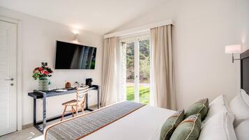 Une chambre à coucher comprenant un lit, un bureau, une chaise, un téléviseur et donnant sur un jardin grâce à une porte coulissante.