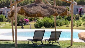 A poolside area with two lounge chairs and a hanging hammock. - Cala Sinzias Resort (Castiadas)