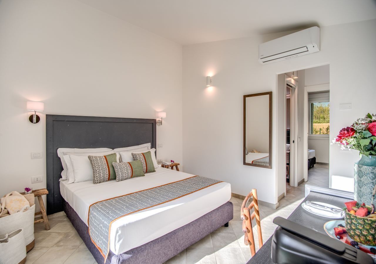 A modern bedroom with a large bed, bedside tables, a mirror, and a dining area with a table set for two.