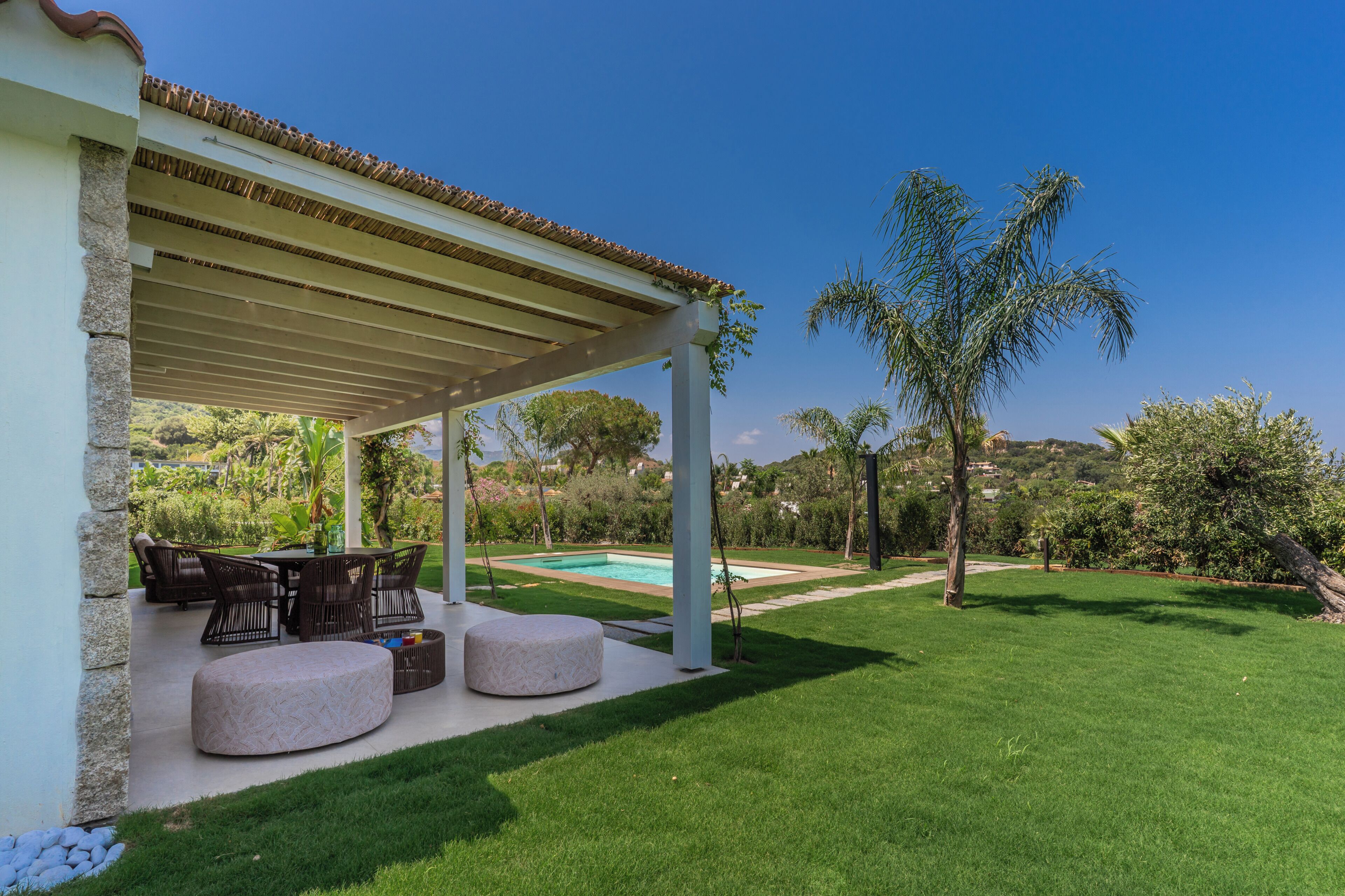 Eine überdachte Terrasse im Freien mit einem Pool, umgeben von einem gepflegten Rasen und verschiedenen Bäumen.