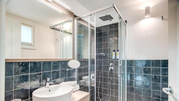 Een moderne badkamer met een groot wit wastafel, een douchecabine van glas en donkere betegelde wanden.